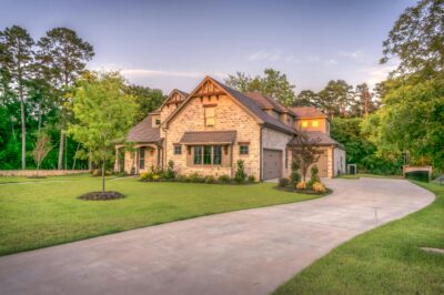 Exterior of a large luxury brick estate with a circular driveway and manicured lawn at sunset, representing the high-value investment properties served by Patricia White in Southeastern North Carolina.