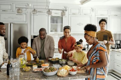 A happy multi-generational Black family laughing and preparing a meal together in a bright, modern white kitchen, illustrating the family-centered real estate services of Devon Denise Shepard.